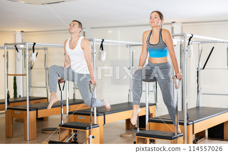 Couple performing Pilates exercises on Wunda chairs in fitness studio Couple performing Pilates exercises on Wunda chairs in fitness studio 114557026