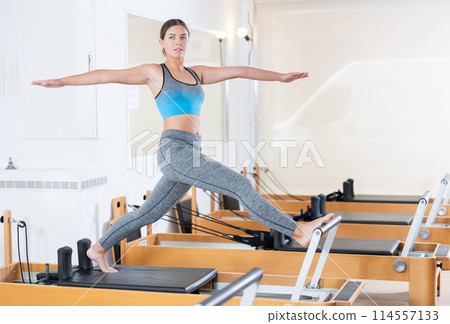 Woman doing pilates exercises lying on pilates workout machines in gym 114557133