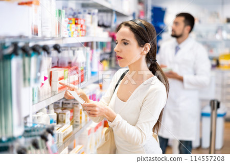 Woman chooses medical products in pharmacy, checking the list on piece of paper Woman chooses medical products in pharmacy, checking the list on piece of paper 114557208