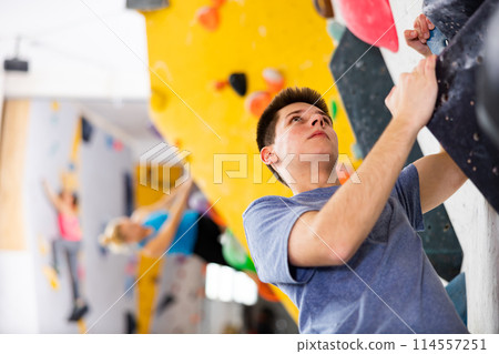 Alpinist practicing indoor rock-climbing on artificial boulder without safety belts Alpinist practicing indoor rock-climbing on artificial boulder without safety belts 114557251
