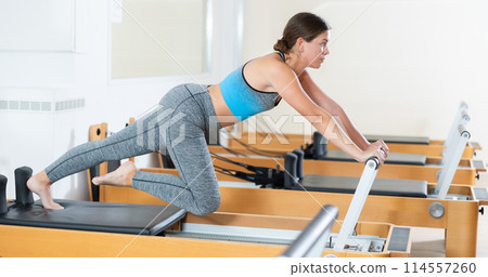 Woman doing pilates exercises lying on pilates workout machines in gym Woman doing pilates exercises lying on pilates workout machines in gym 114557260