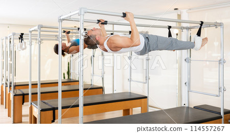 Man performing inverted hanging pull-ups on Pilates trapeze table Man performing inverted hanging pull-ups on Pilates trapeze table 114557267