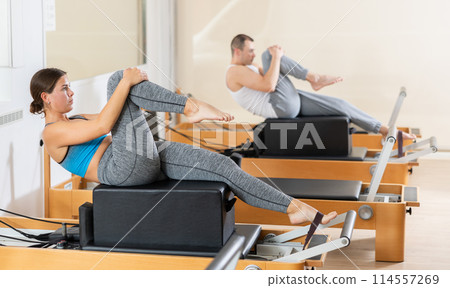 Female athletic girl doing stretching on pilates machine in pilates studio Female athletic girl doing stretching on pilates machine in pilates studio 114557269