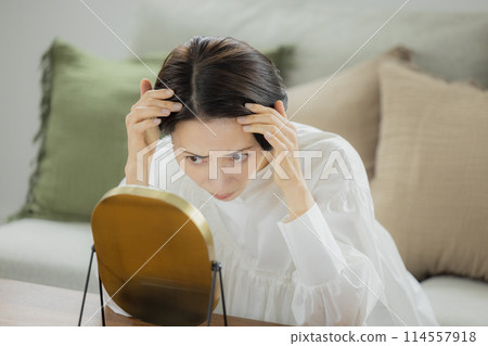 Middle-aged woman looking in the mirror in the living room 114557918