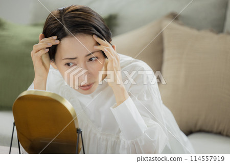Middle-aged woman looking in the mirror in the living room 114557919
