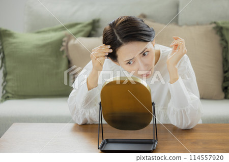 Middle-aged woman looking in the mirror in the living room 114557920