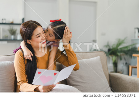 Happy mother's day. Mother receiving a handmade card from her daughter in living room at home. Happy mother's day. Mother receiving a handmade card from her daughter in living room at home. 114558371