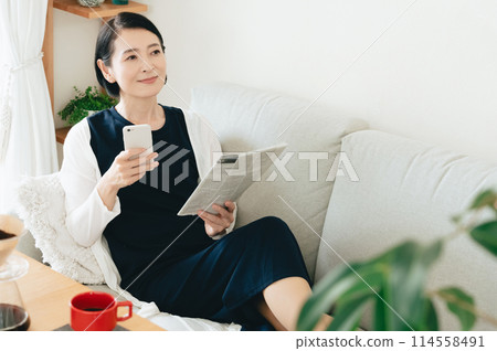 A middle-aged woman reading a smartphone and an English newspaper 114558491