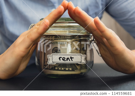 Unrecognizable woman holding Saving Money In Glass Jar filled with Dollars banknotes. RENT transcription in front of jar. Managing personal finances extra income for future insecurity Unrecognizable woman holding Saving Money In Glass Jar filled with Dollars banknotes. RENT transcription in front of jar. Managing personal finances extra income for future insecurity 114559681