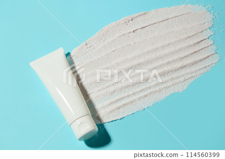A thin layer of white cream is spread evenly on light blue surface with a cosmetic tube without label to advertise skin care products. Top view photo with empty space for design A thin layer of white cream is spread evenly on light blue surface with a cosmetic tube without label to advertise skin care products. Top view photo with empty space for design 114560399