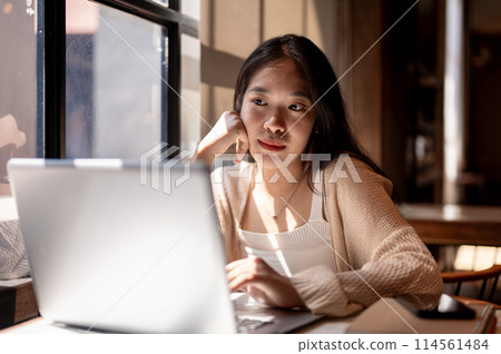 Young thoughtful Asian woman working remotely at a coffee shop, pensive planning about her job. 114561484