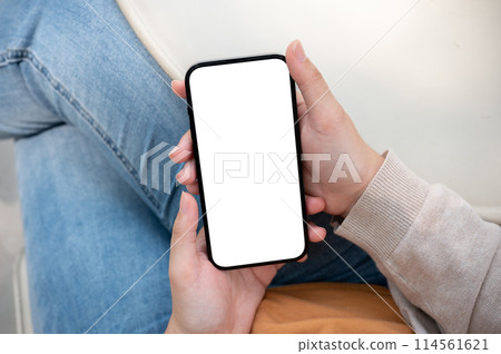 A close-up image of a woman in jeans sits outdoors on a sunny day and uses her smartphone. A close-up image of a woman in jeans sits outdoors on a sunny day and uses her smartphone. 114561621