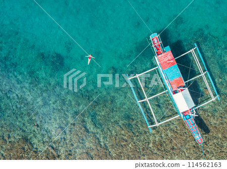 Aerial View of a Woman in Red Swimsuit Floating Serenely on the Crystal Clear Ocean Waters During Midday Aerial View of a Woman in Red Swimsuit Floating Serenely on the Crystal Clear Ocean Waters During Midday 114562163