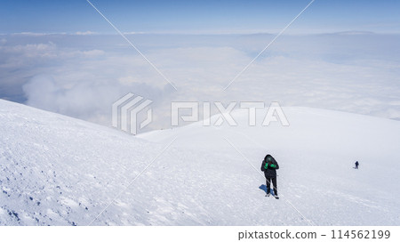 Mountaineers walking towards the snowy mountain summit above the clouds, Mount Ararat in Turkey 114562199