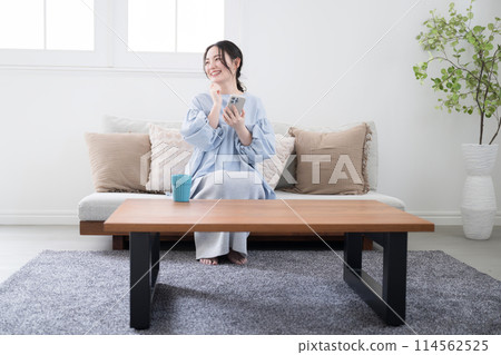A young woman thinking with a smartphone in a beautiful living room 114562525