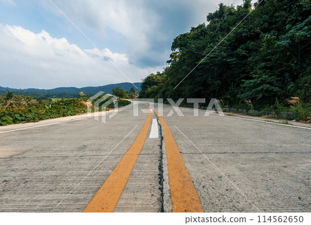 Country road with trees against the blue sky and clouds. A serene asphalt road winds through lush green mountains 114562650