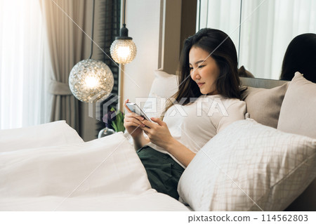 Asian woman in bed checking social apps with smartphone in morning. Asian woman in bed checking social apps with smartphone in morning. 114562803