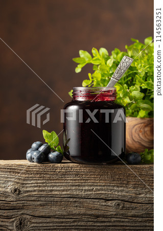 Jar of blueberry jam with fresh berries on an old wooden table. 114563251