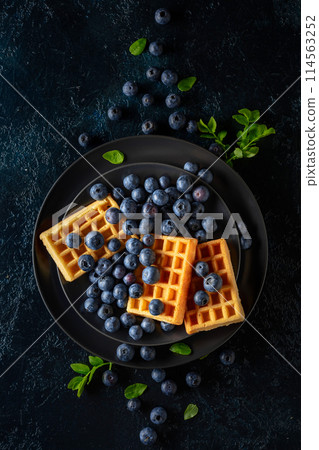 Belgian waffles with blueberries on a black plate. 114563252