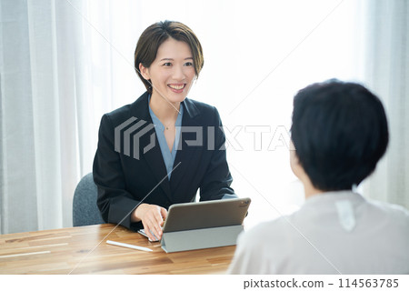 A woman in a suit explaining to a woman in plain clothes 114563785