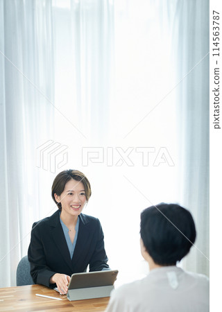 A woman in a suit explaining to a woman in plain clothes 114563787