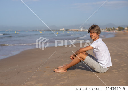 Handsome smiling teenager boy sitting at the beach and enjoy a summer vacation. 114564049