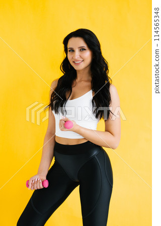 Sporty young woman with dumbbells on yellow background Sporty young woman with dumbbells on yellow background 114565348