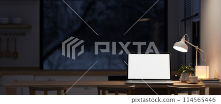 A laptop on a dining table in a contemporary kitchen at night with a dim light from a floor lamp. A laptop on a dining table in a contemporary kitchen at night with a dim light from a floor lamp. 114565446