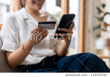 A cropped image of a woman holding a credit card and her smartphone on a sofa in the living room. 114565587