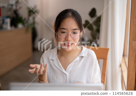 A young Asian woman is talking, having an online meeting while working remotely at a coffee shop. A young Asian woman is talking, having an online meeting while working remotely at a coffee shop. 114565628