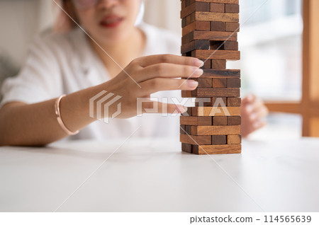 A woman pays her attention on playing a wooden block game at a table, moving a wooden block. A woman pays her attention on playing a wooden block game at a table, moving a wooden block. 114565639
