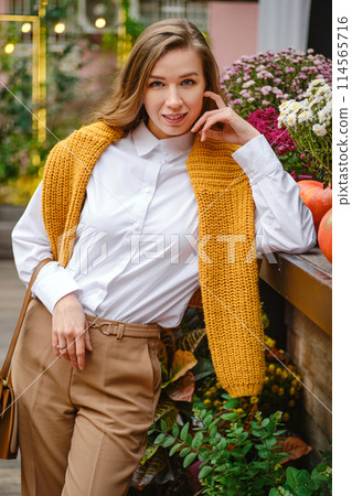 Portrait of lovely woman at an autumn fair leaning on a wooden display table 114565716
