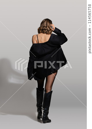Back view of a woman taking off blazer in leather riding boots in studio Back view of a woman taking off blazer in leather riding boots in studio 114565758
