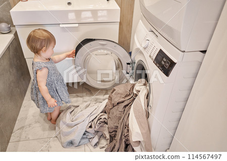 changing of bed linen while House cleaning. Happy baby girl one and a half, helper are having fun and smiling while in a bright apartment. Helps parents change bed linen and do laundry in the washing changing of bed linen while House cleaning. Happy baby girl one and a half, helper are having fun and smiling while in a bright apartment. Helps parents change bed linen and do laundry in the washing 114567497
