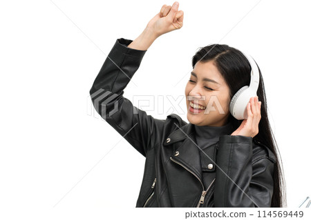 A young woman wearing a leather jacket gets excited listening to music through headphones 114569449