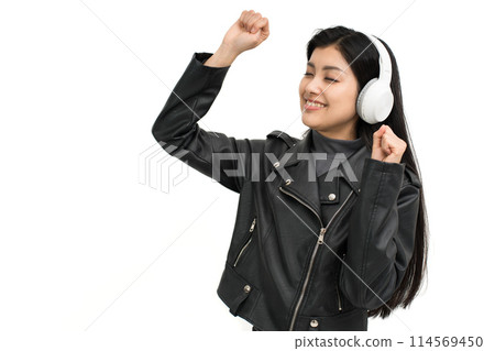 A young woman wearing a leather jacket gets excited listening to music through headphones 114569450