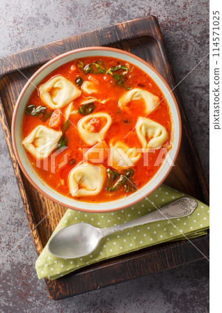 Tomato tortellini soup with vegetables and spinach close-up in a plate. Vertical top view 114571025