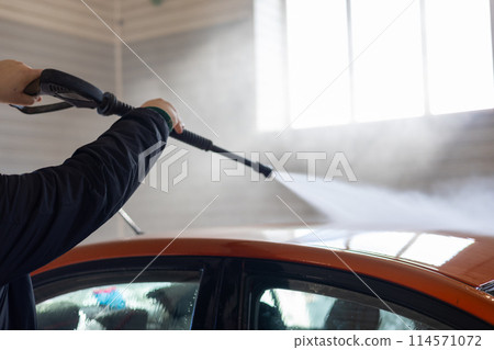 A man holds a gun in his hands and washes his car at a car wash. A man washes dirt off the roof of his orange car. With the help of a powerful water gun, a man can easily remove dirt from his car. A man holds a gun in his hands and washes his car at a car wash. A man washes dirt off the roof of his orange car. With the help of a powerful water gun, a man can easily remove dirt from his car. 114571072