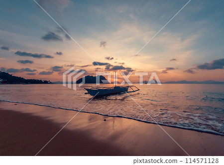 Stunning sunset over serene beach with boat in calm waters, evening time. 114571128