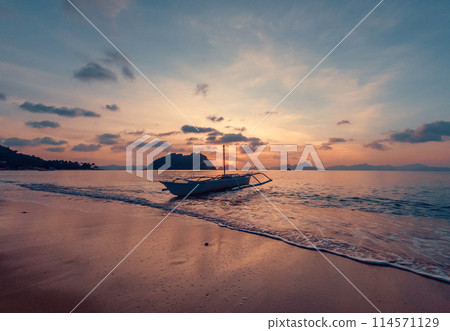 Stunning sunset over serene beach with boat in calm waters, evening time. 114571129