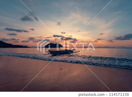 Stunning sunset over serene beach with boat in calm waters, evening time. 114571130