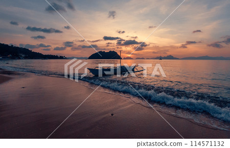 Stunning sunset over serene beach with boat in calm waters, evening time. 114571132