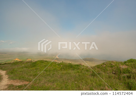 A foggy day with a cloudy sky and a grassy hill. The sky is blue and the clouds are white. 114572404