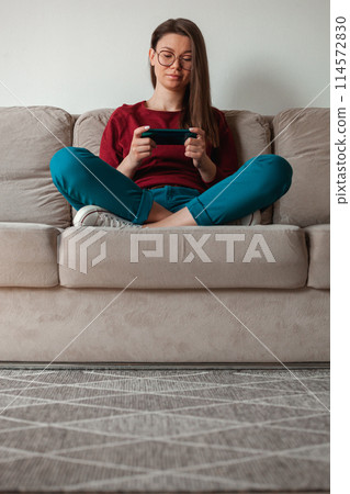 Woman using mobile phone, holding in hands sitting on sofa Woman using mobile phone, holding in hands sitting on sofa 114572830
