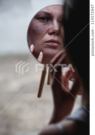 Domestic violence, abuse woman with bruise on face by the window looks in the mirror Domestic violence, abuse woman with bruise on face by the window looks in the mirror 114572847
