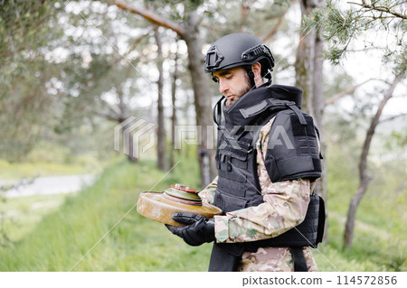 A man in a special suit works with a detector and found an explosive device. A man tries to neutralize an anti-tank mine 114572856