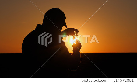 Silhouette of a farmer examining seedlings in the field. Back view Silhouette of a farmer examining seedlings in the field. Back view 114572891