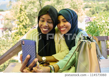 Middle Eastern Muslim Women Capturing Selfies in Serene Surroundings 114573060