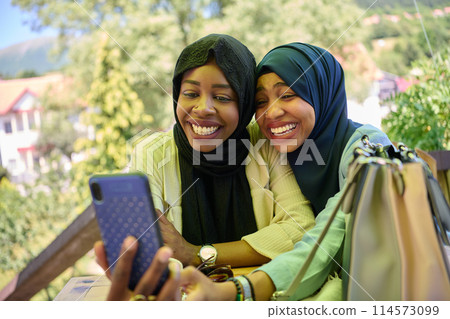 Middle Eastern Muslim Women Capturing Selfies in Serene Surroundings 114573099