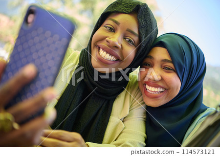 Middle Eastern Muslim Women Capturing Selfies in Serene Surroundings 114573121